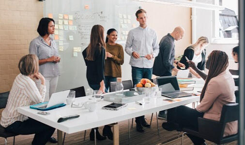 Team of individuals sitting around a table brainstorming ideas and organizing thoughts using post-it notes on a wall.